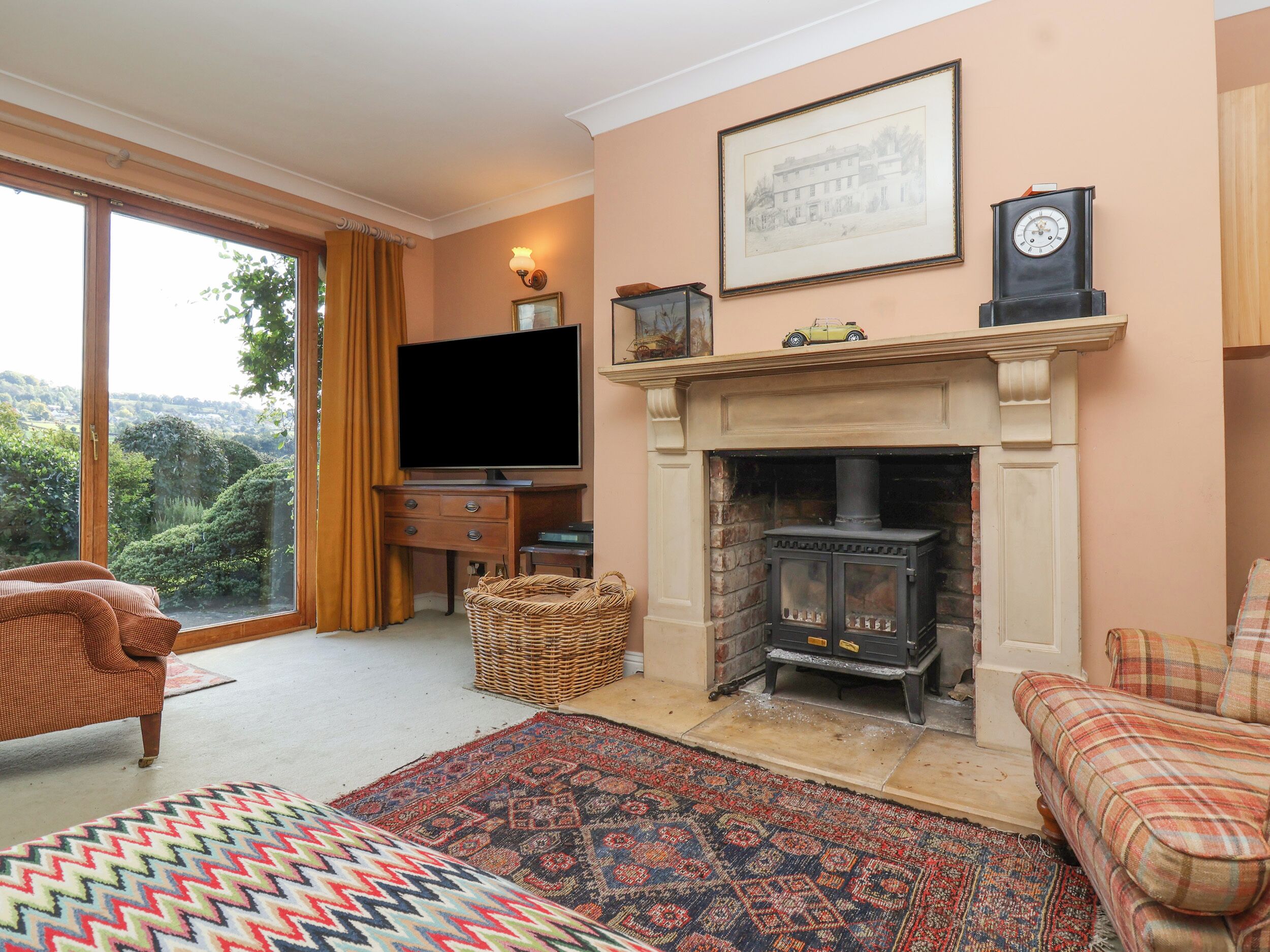 A cozy living room with a fireplace, a television, and a large window overlooking greenery.