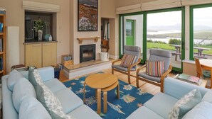 Un salón amplio con sofá, sillas, chimenea y vistas al exterior.