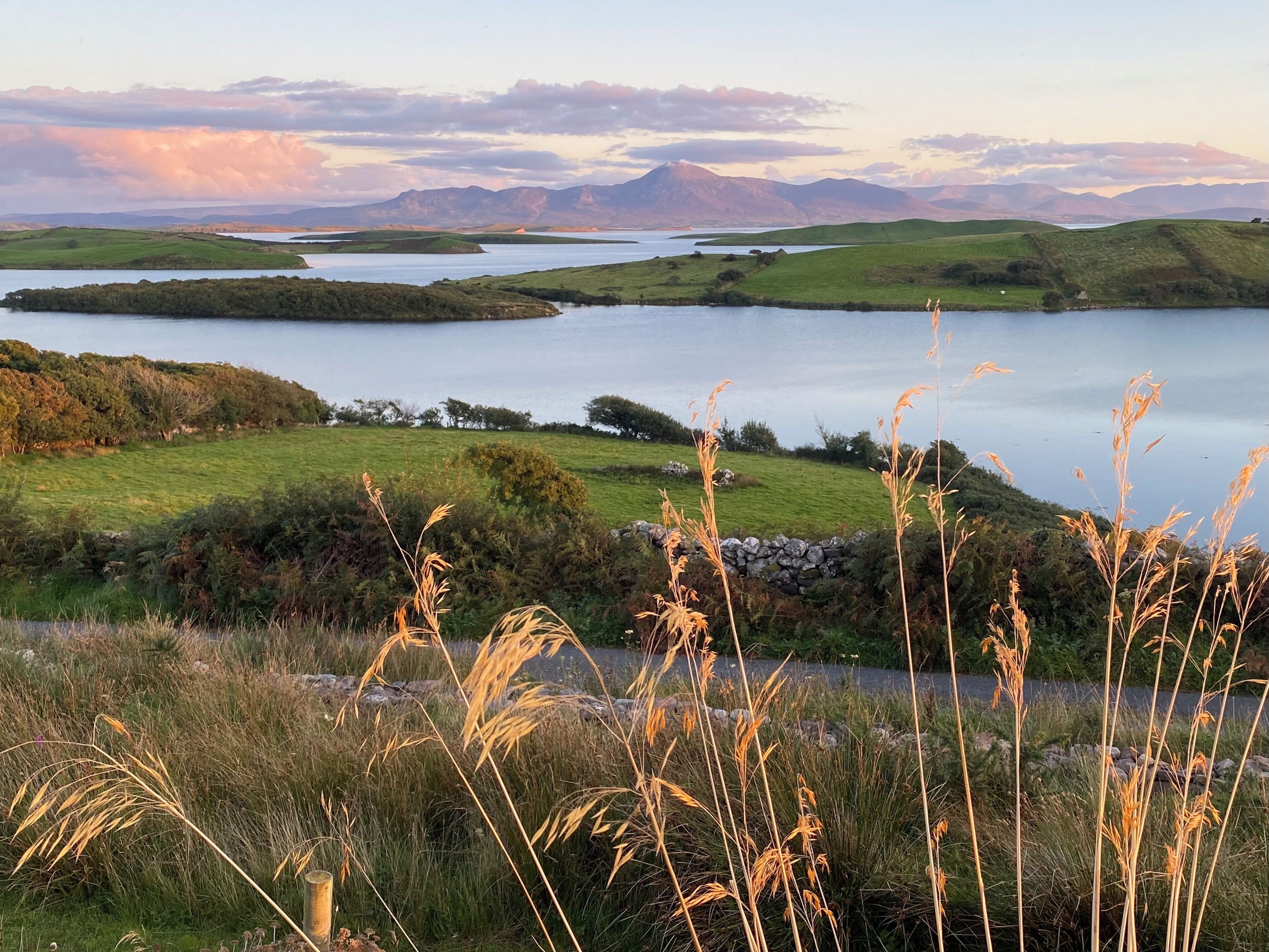A lakeside landscape with grassy fields and a stone wall.