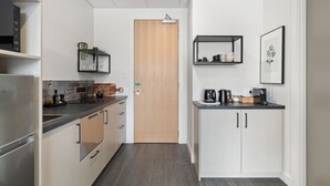 Een moderne keuken met een inbouwoven, een koffieapparaat en een klein schap met keukengerei.