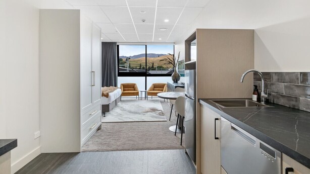 Een moderne keuken met een groot raam, een eethoek met een tafel en stoelen, en een slaapkamer met een bed en uitzicht op de heuvels.