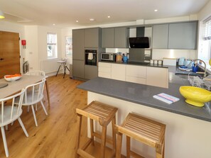 Een moderne keuken met grijze kastjes, een zwarte magnetron en een houten eettafel met witte stoelen.