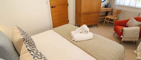 A bedroom with a bed, a wooden wardrobe, a desk, a red armchair, and a window with curtains.