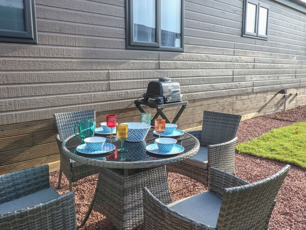 Un espace de restauration en plein air avec des chaises en osier et une table ronde, un barbecue et de la vaisselle colorée.