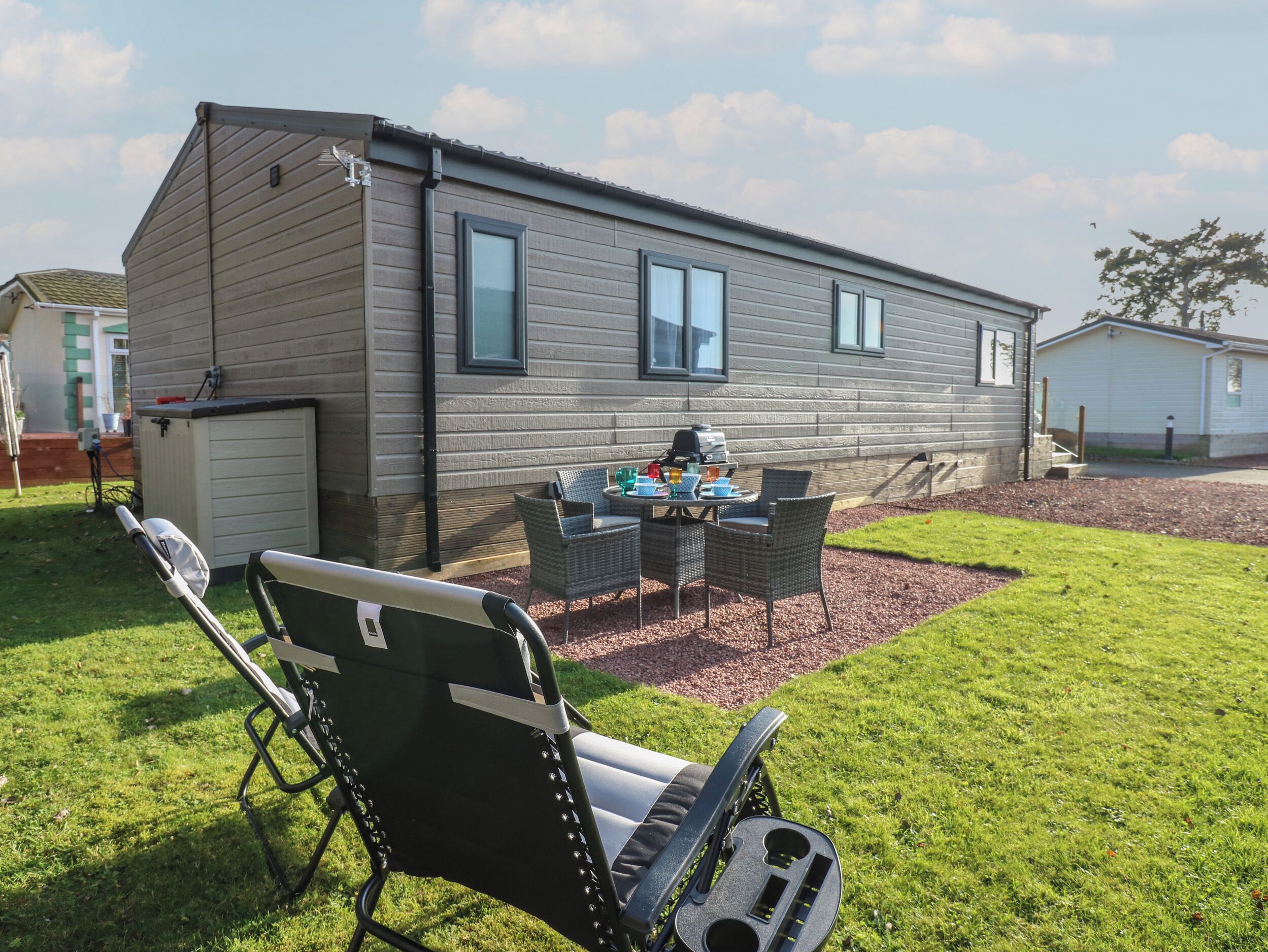 Una casa móvil de un nivel con un patio, una parrilla y mobiliario de exterior.