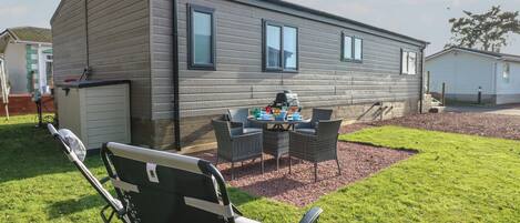Una casa móvil de un nivel con un patio, una parrilla y mobiliario de exterior.