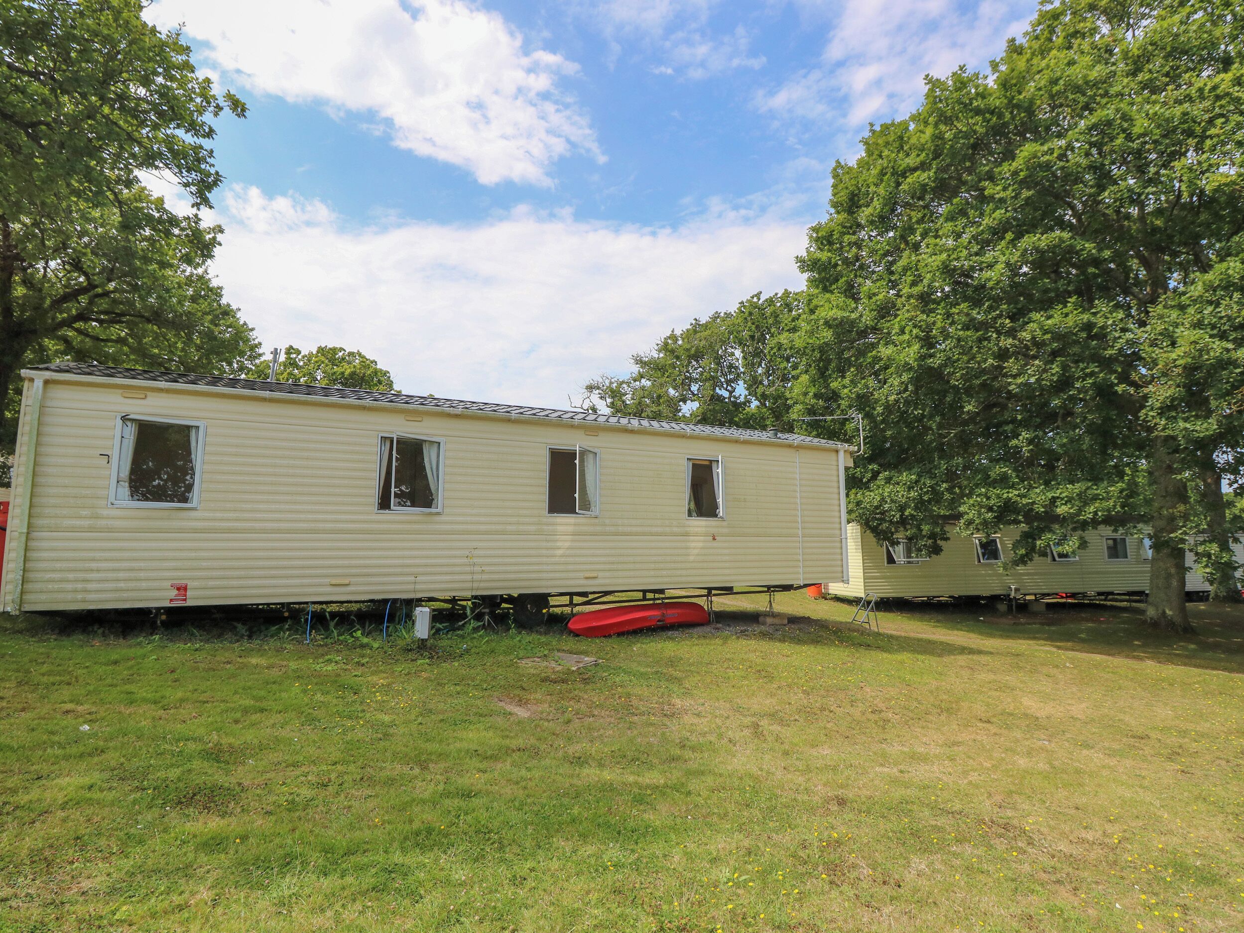 A mobile home with a small window, a red object on the ground, and a tree in the background.