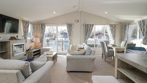 A spacious living area with a sofa, armchair, and a dining table. A television is mounted on the wall, and there is a fireplace. - The Three Bears Lodge, Coniston Drive 11 (Carnforth)