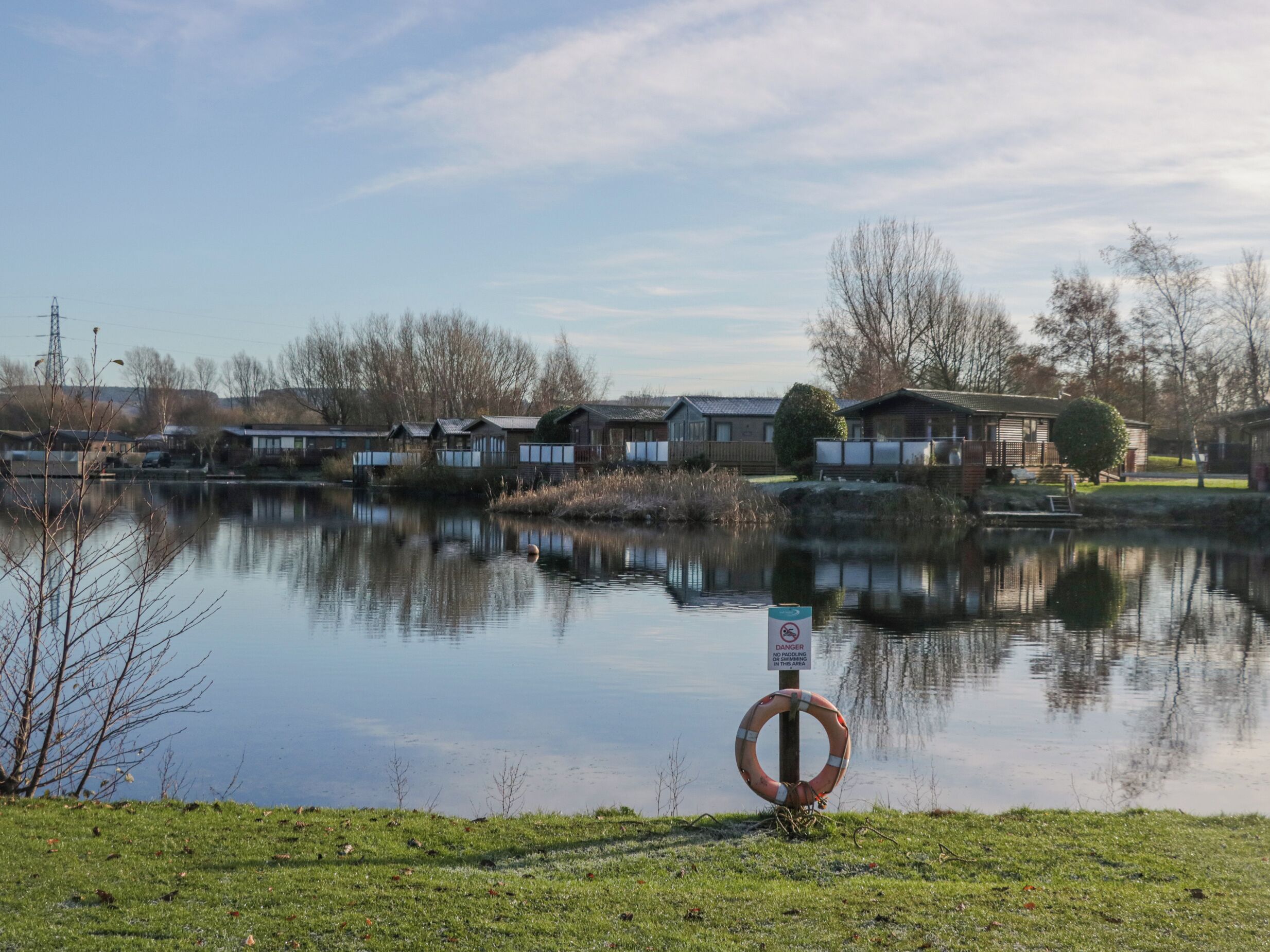 A calm lake with a no-swimming sign, surrounded by buildings and trees.