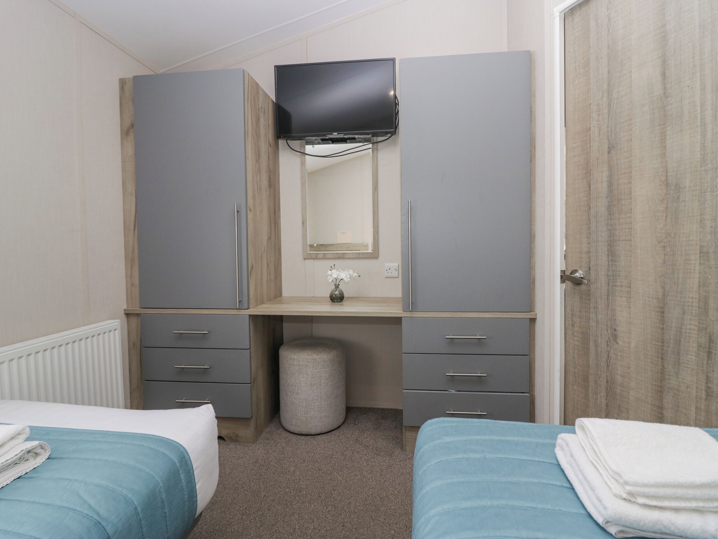Un dormitorio con dos camas, un aparador, un espejo y un televisor.