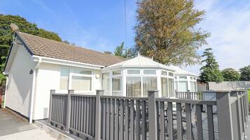 A caravan with a fenced patio area, a tiled roof, and a large tree in the background.