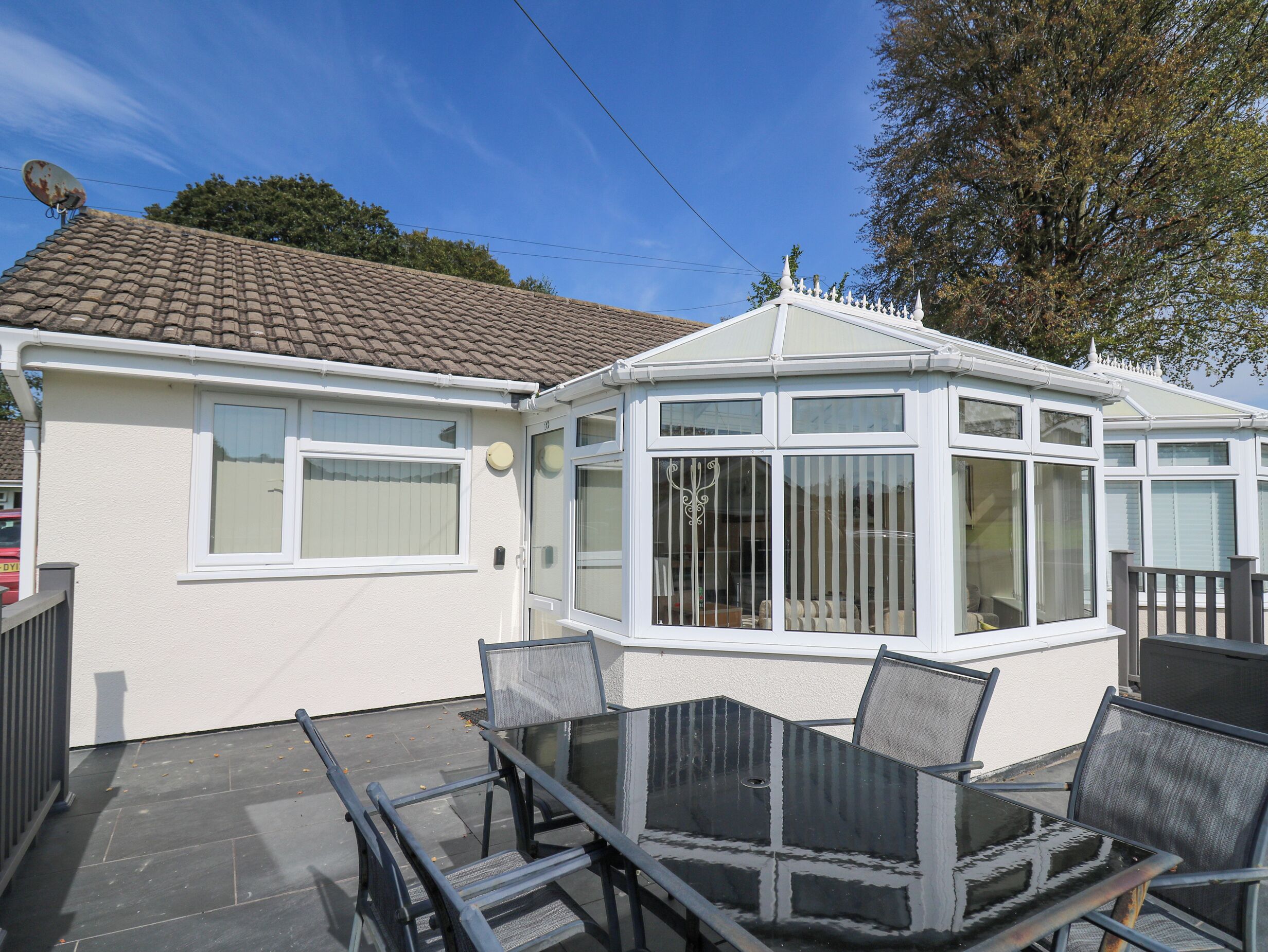 A conservatory with a glass roof, white walls, and a tiled roof.