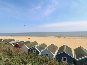 Beach huts with sloped roofs, a sandy beach, and the sea in the background. - Iona Cottage (Reydon)
