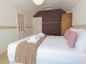 A bedroom with a bed, a wooden wardrobe, and a door. - Iona Cottage (Reydon)