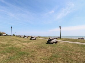 A grassy field with several cannons aligned in a row, a pathway, and a bench with people sitting. - Iona Cottage (Reydon)