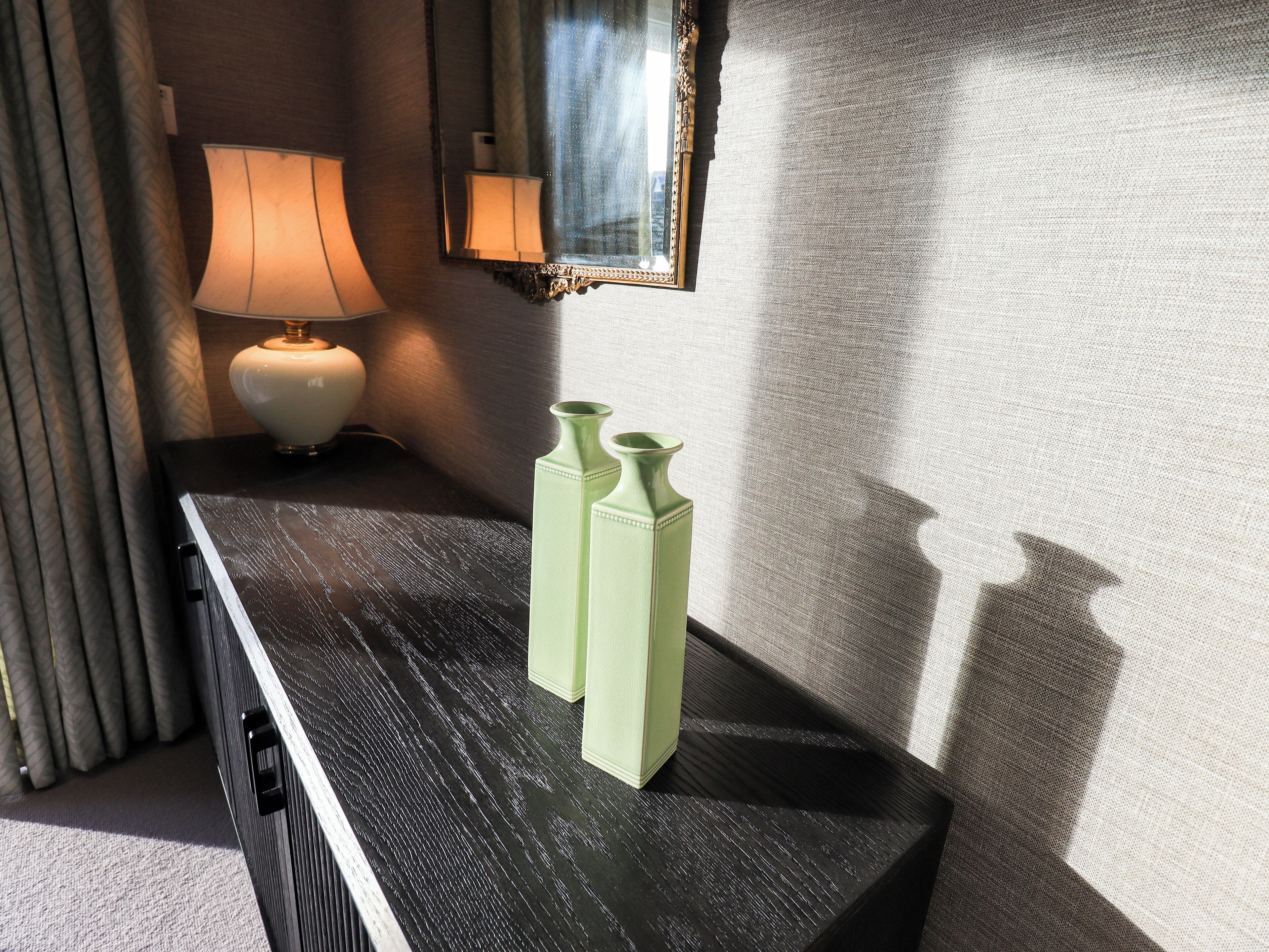 A dark wooden console table with two green vases, a lamp, and a mirror on the wall.
