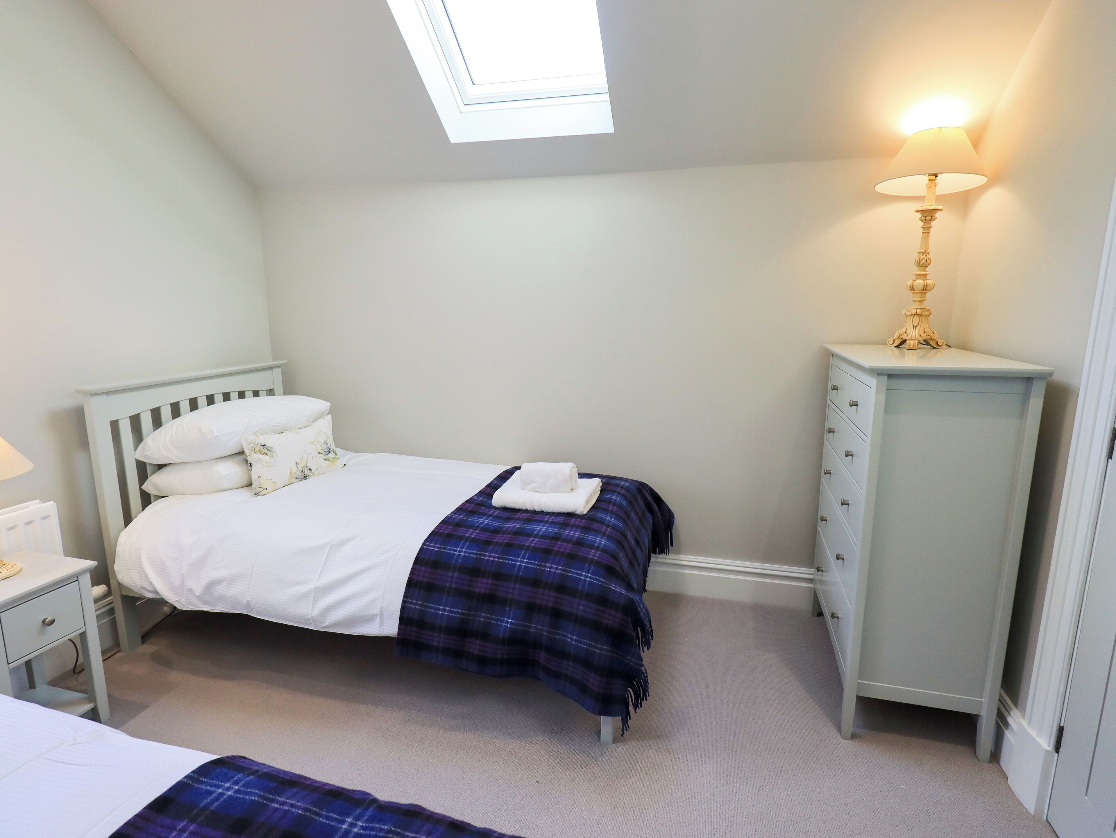 Une chambre à coucher comprenant un lit, une table de chevet, une commode, une lampe et une lucarne.