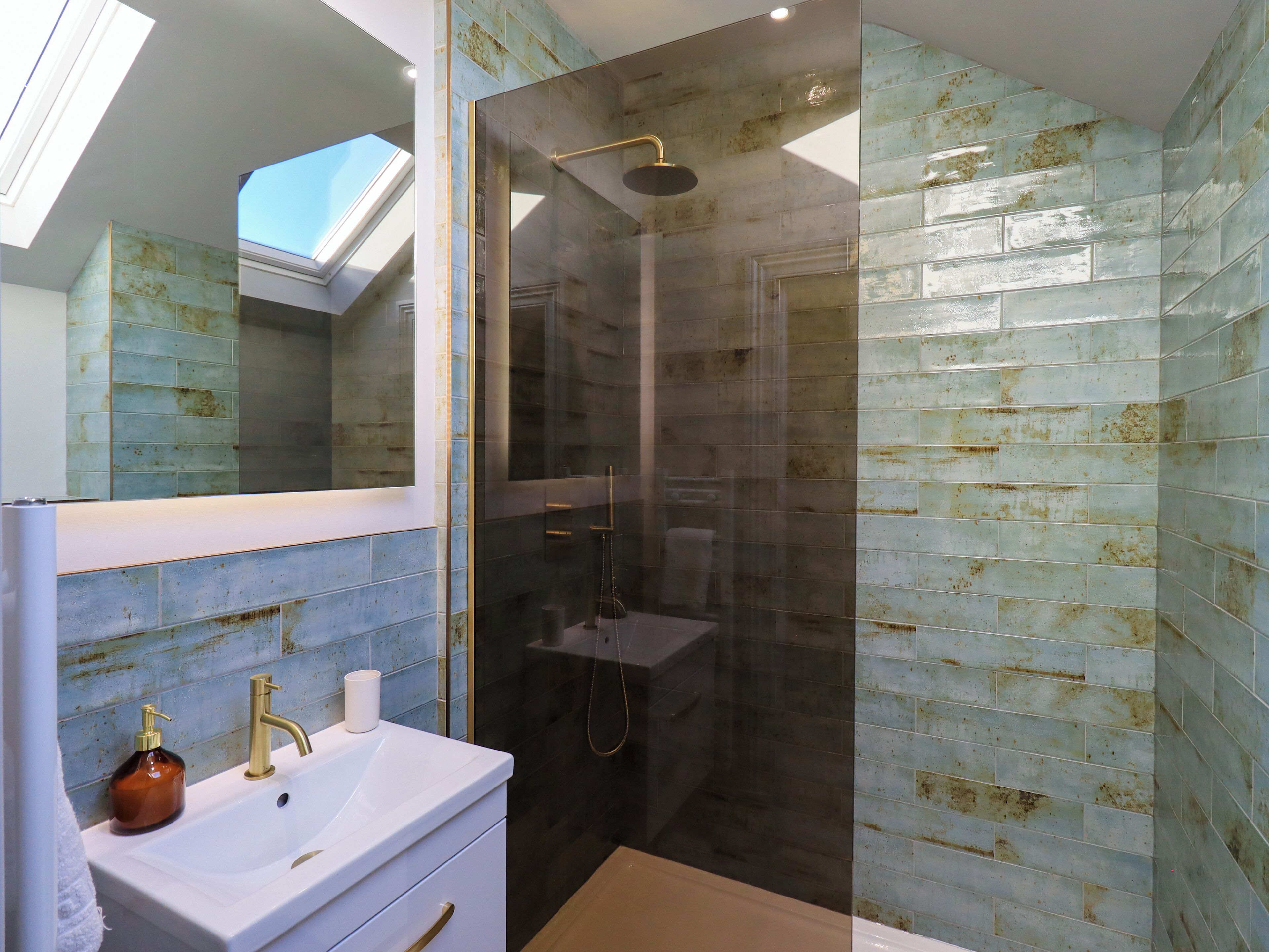 A modern bathroom with a skylight, a glass-enclosed shower, and a sink with a gold faucet.