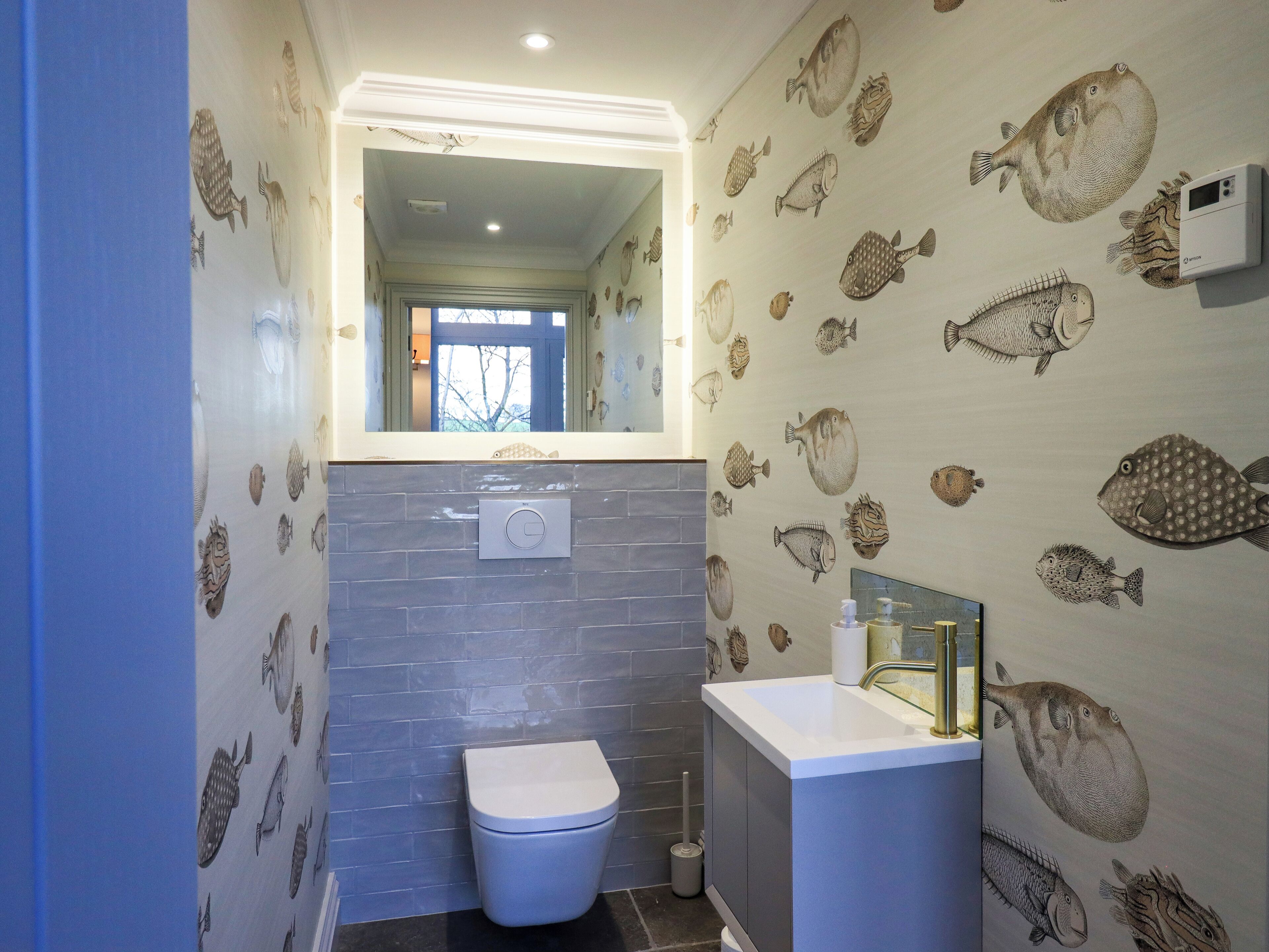 Um banheiro com papel de parede com tema de peixes, uma pia moderna e um vaso sanitário.