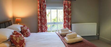 A bedroom with a bed, pillows, a bedside lamp, a window with curtains, and a radiator.
