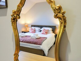 Cama bem arrumada com lençóis brancos e almofadas florais vermelhas, luminária de cabeceira e mesa de cabeceira de madeira.
