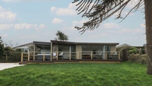 A modern house with a covered patio area, a visible garage, and a well-maintained lawn. - The Bay (Tyn-y-Gongl)