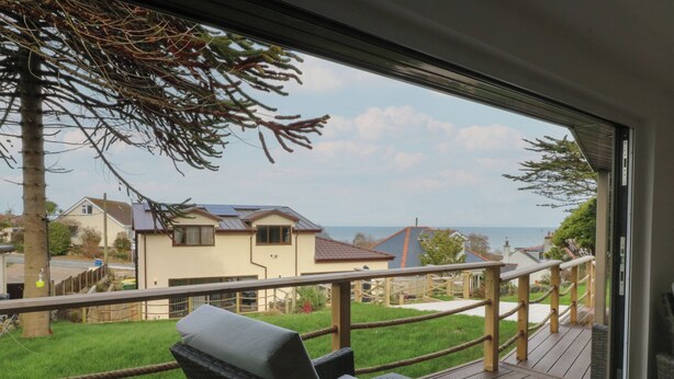 A balcony with wicker furniture, a view of houses, and a grassy area. - The Bay (Tyn-y-Gongl)