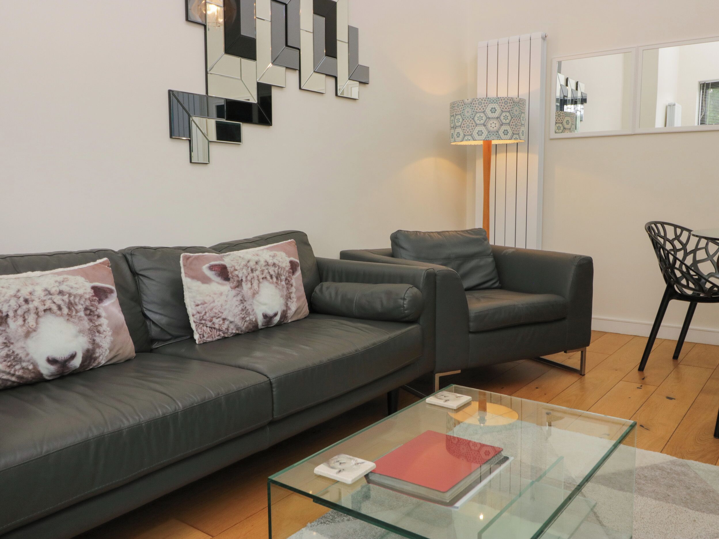 Un salón moderno con un sofá gris, dos cojines, una mesa de centro de cristal y una lámpara.