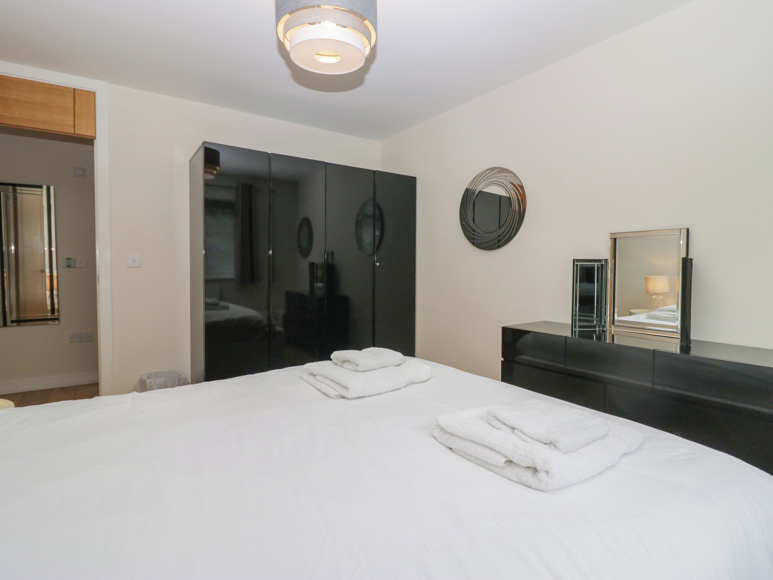 A modern bedroom with a large bed, a wardrobe, a mirror, and a bedside table.