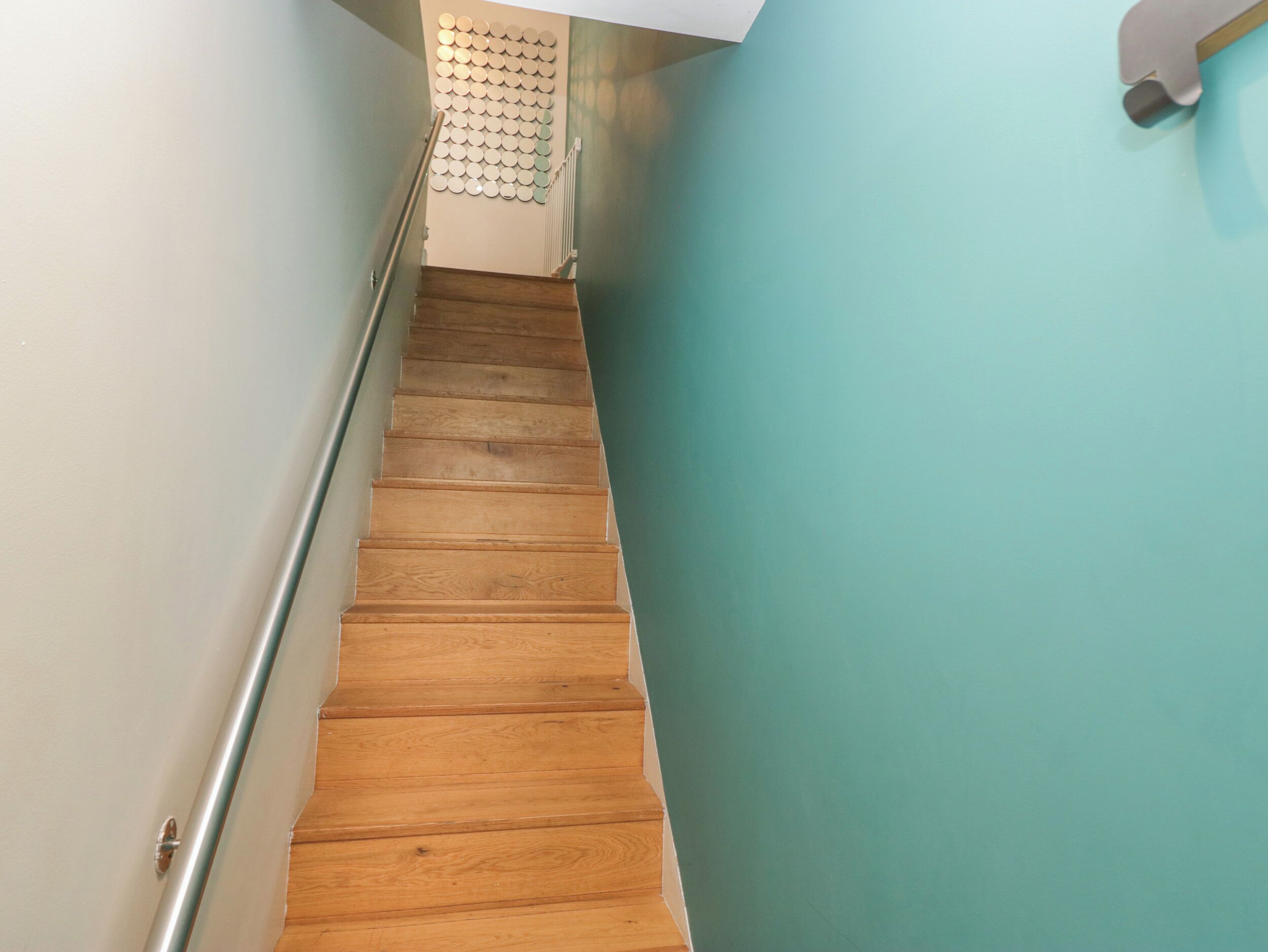 A wooden staircase with a metal handrail, leading to a landing with a wall-mounted circular object.
