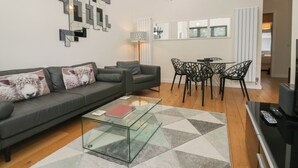 A modern living room with a grey sofa, a glass coffee table, and a dining area with black chairs. - 12 Blue Hill Park (Ambleside)