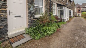 A stone cottage with a white door, a number plaque, and a gravel driveway.