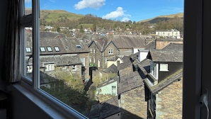 A view through a window of a town with stone buildings, a river, and hills in the background.