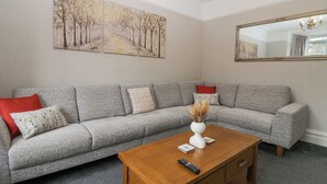 A living room with a grey sofa, a wooden coffee table, and a painting of trees on the wall. - Park Beck 3 (Windermere)