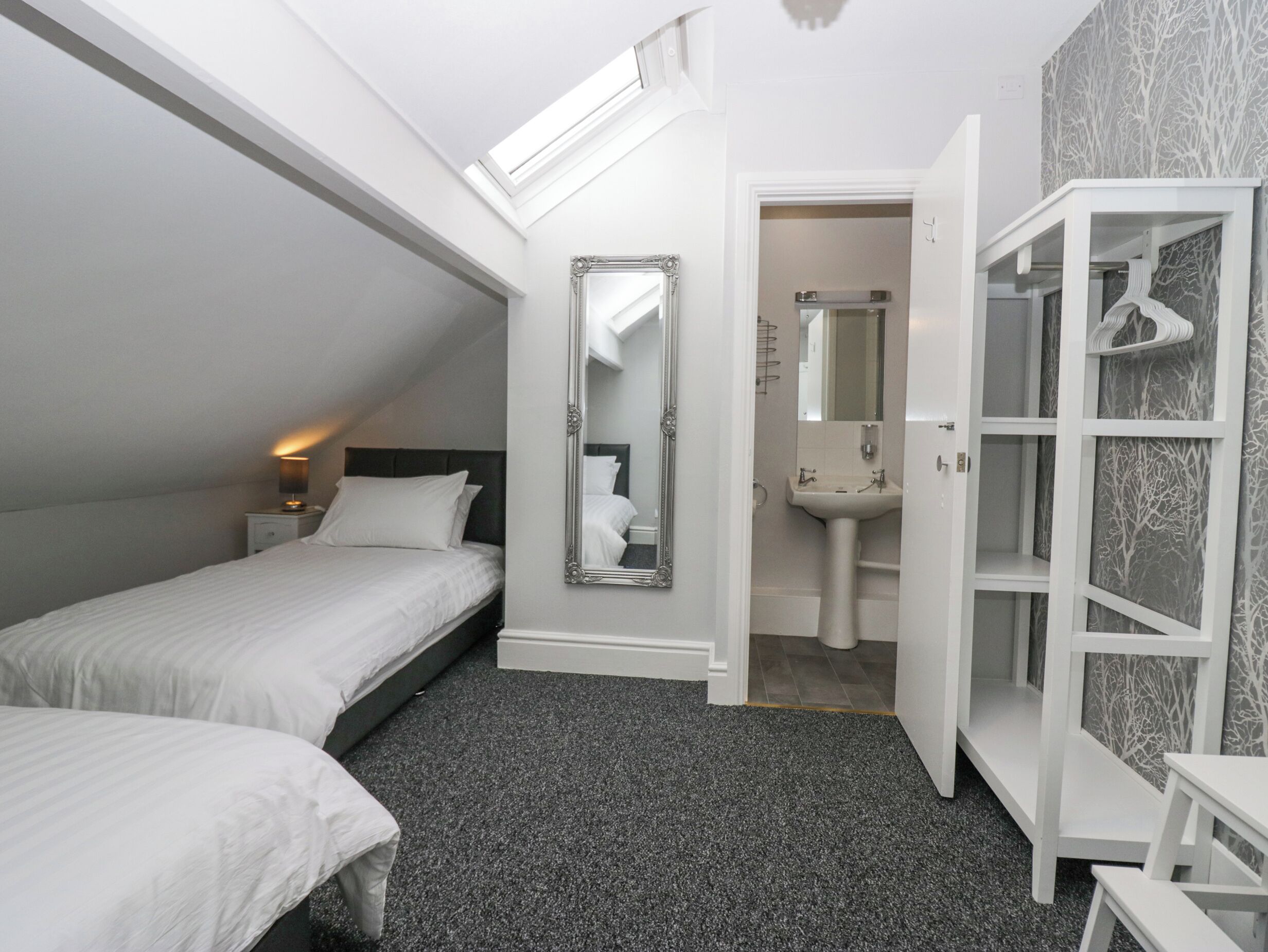 Ein Schlafzimmer mit zwei Betten, einem großen Spiegel, einem Badezimmer mit Waschbecken und einem Kleiderschrank mit Tür im Baumdekor.