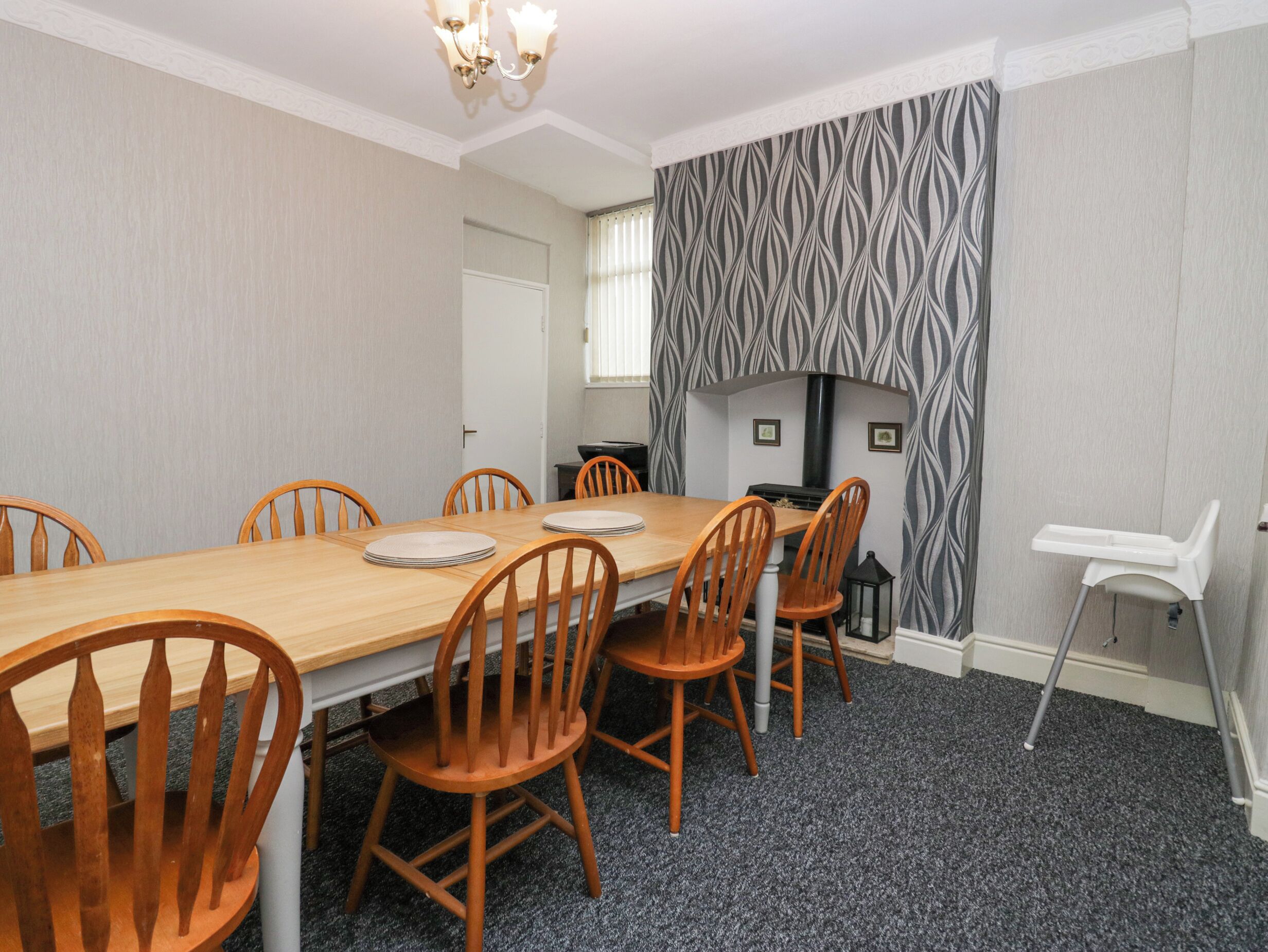 Een eetkamer met een houten tafel en stoelen, een open haard en een witte stoel.