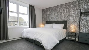 A bedroom with a large bed, grey curtains, a window, a patterned wall, and bedside lamps. - Park Beck 3 (Windermere)
