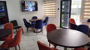Una sala de conferencias con un televisor montado en la pared, una mesa redonda y sillas con tapicería en tonos rojo y azul.