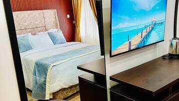 A hotel room with a bed, a TV, a desk, and a small table.