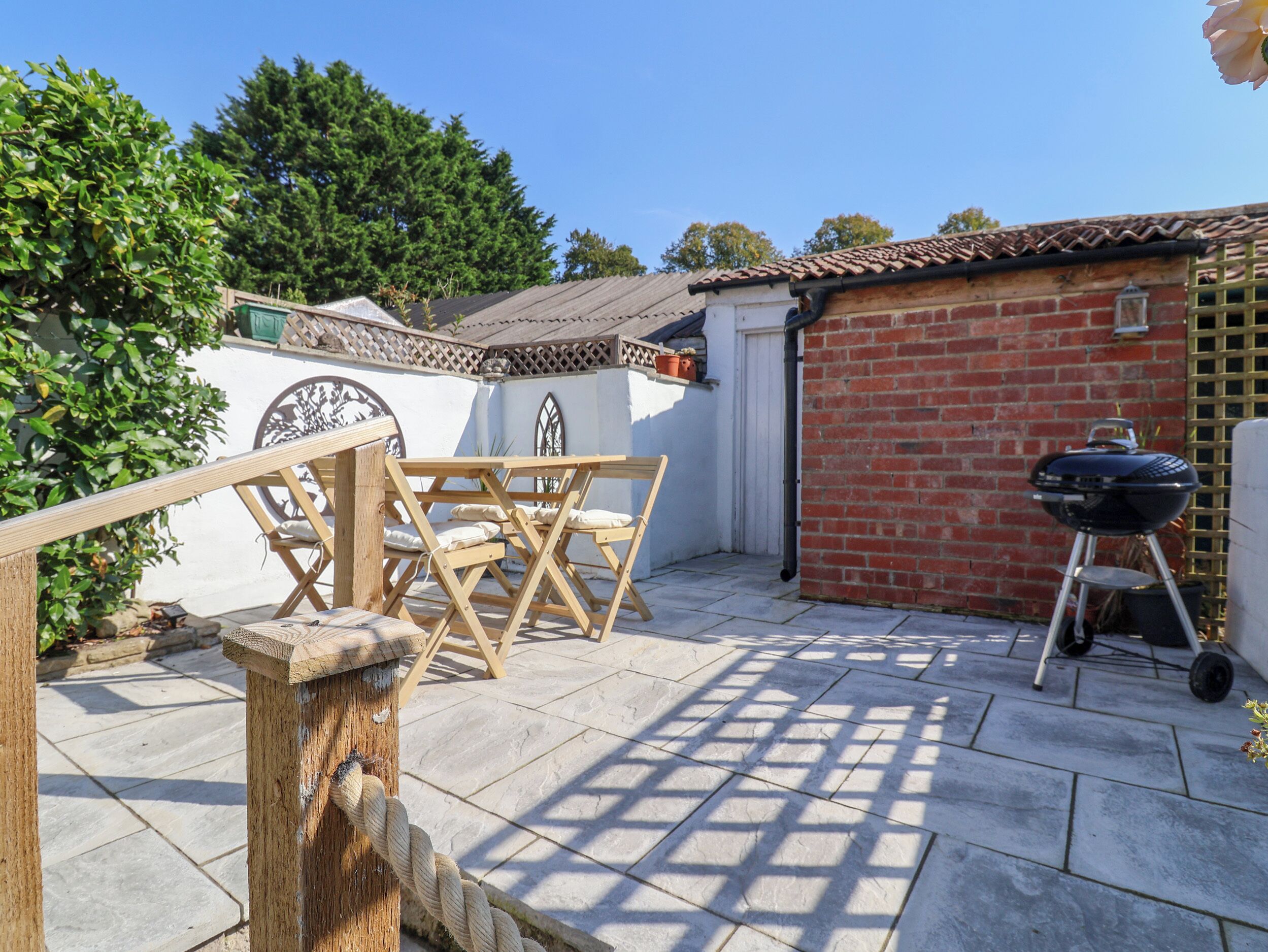 Een terras met een houten tafel en stoelen, een barbecue en een bakstenen muur.