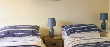 A hotel room with two beds, each with striped bedding, a nightstand with a lamp, and a framed picture of red flowers on the wall.