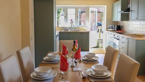 A dining area with a table set for four, a kitchen in the background, and a view of a garden through the window. - 30 Fleet Street (Beaminster)