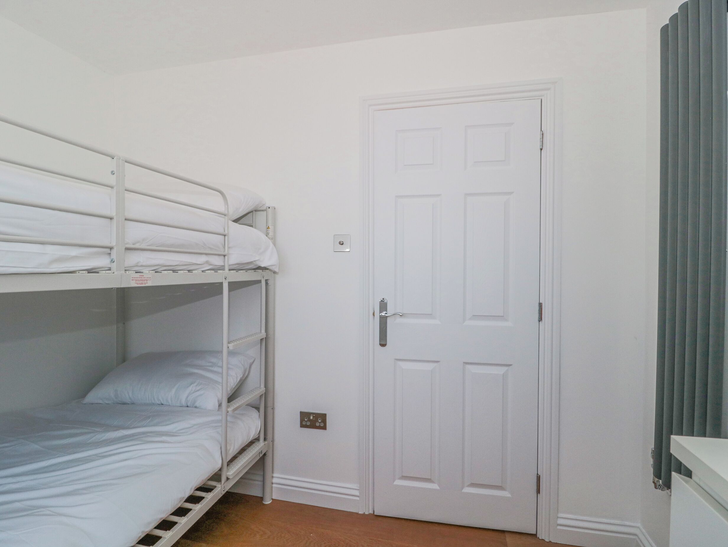 A bunk bed room with a white door and a light switch on the wall.