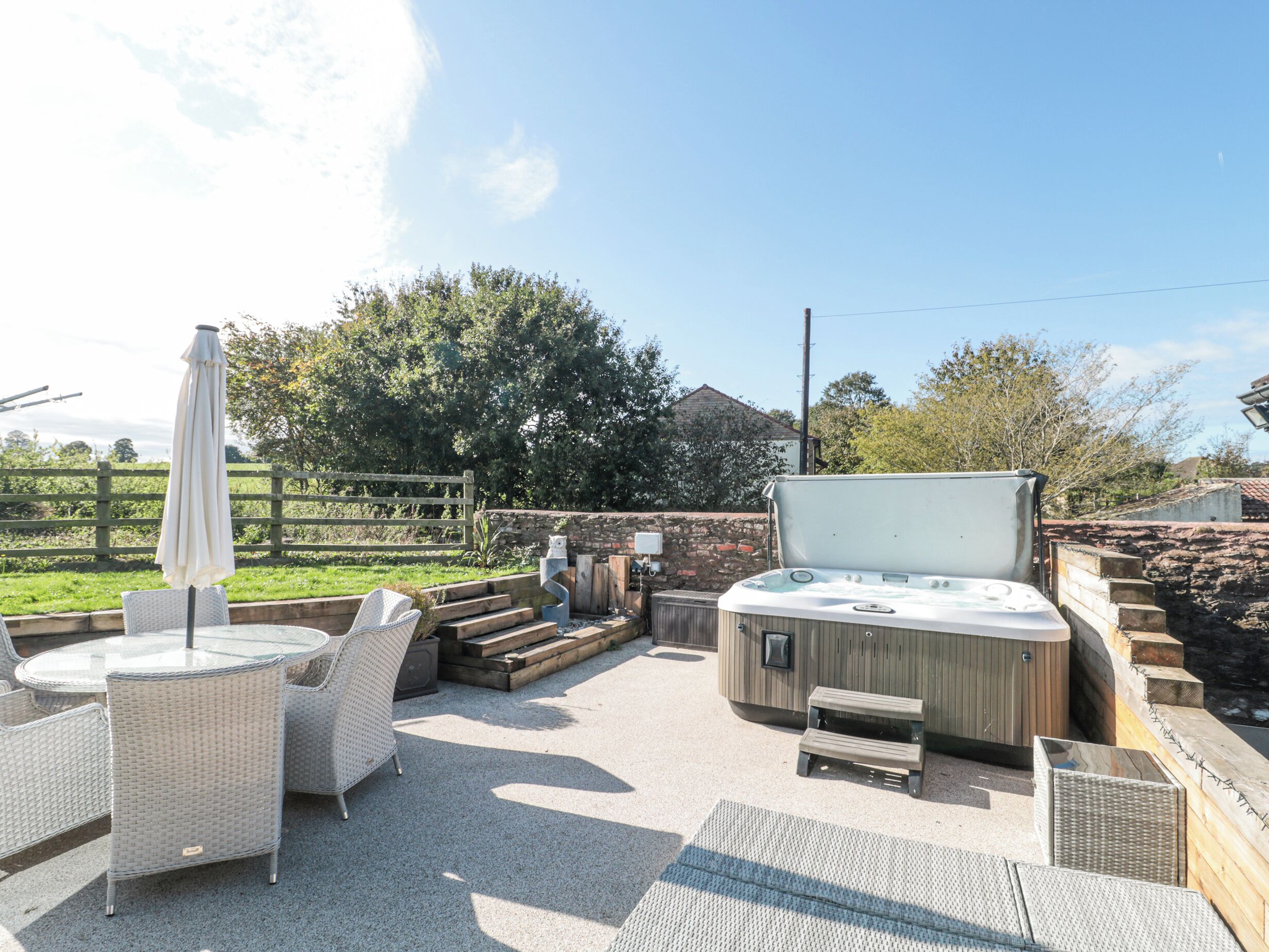 An outdoor patio area with wicker furniture, a hot tub, and a wooden fence.