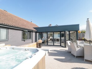 A modern outdoor patio with a hot tub, wicker furniture, and a glass-enclosed seating area. - Orchard Leigh (Bridgwater)