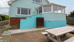 A two-story house with a light blue exterior, a wooden bench, and a flower pot in the front yard. - Carousel (Haverfordwest)