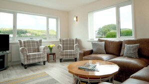 A living room with a brown leather sofa, two plaid armchairs, a coffee table, and a television. - Carousel (Haverfordwest)