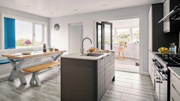 A modern kitchen with a central island, built-in oven, and a dining area with a bench. - Carousel (Haverfordwest)