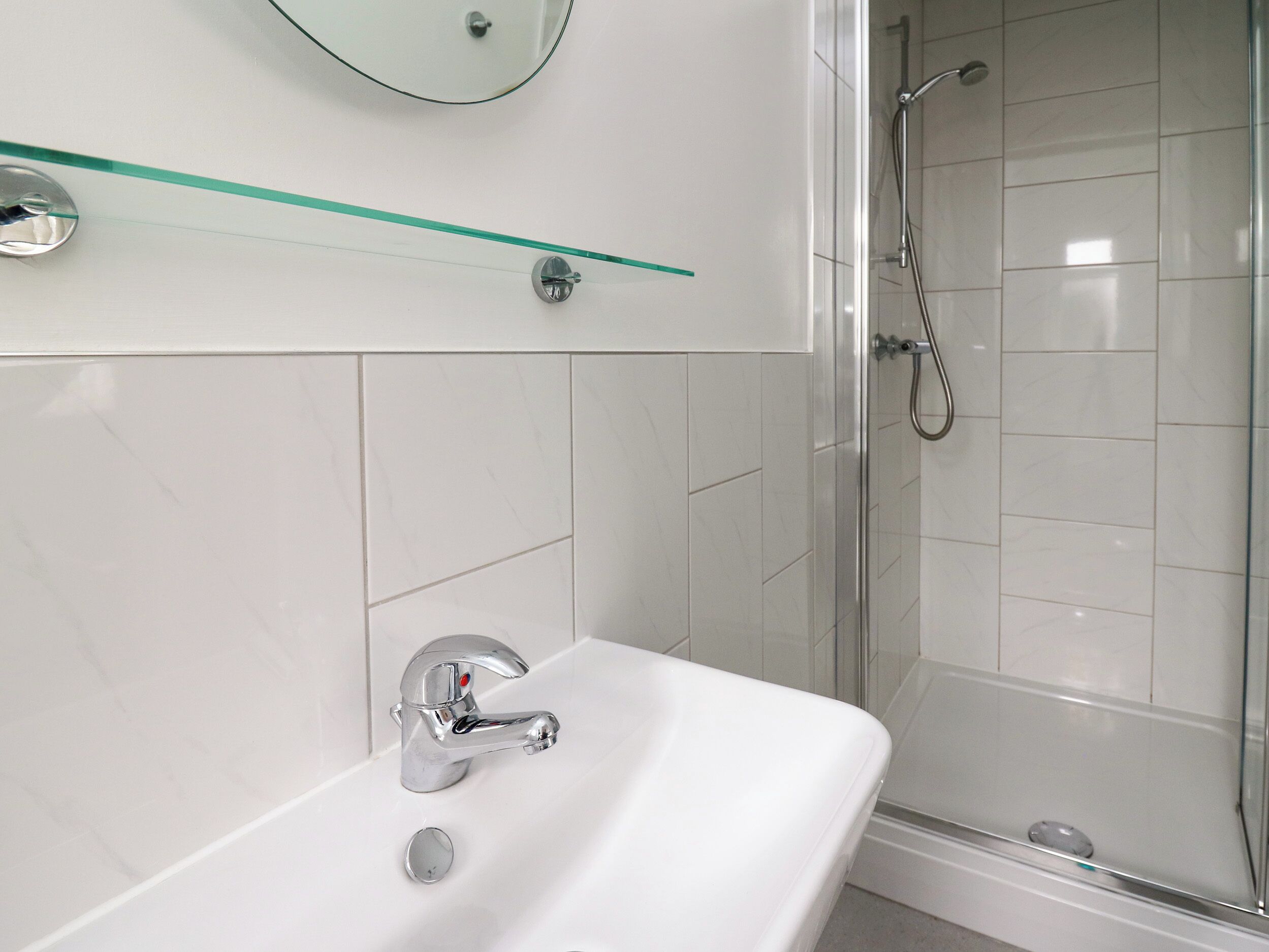 Een moderne badkamer met een wit wastafelmeubel, een chromen kraan en een glazen plank erboven.