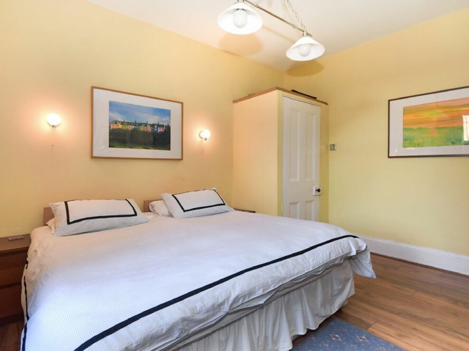 Un dormitorio con una cama, dos lámparas de pared, una puerta y dos cuadros enmarcados.